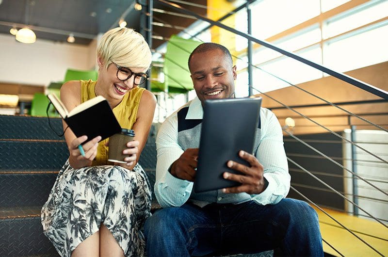 Two persons sitting on stairs while holding a book and coffee